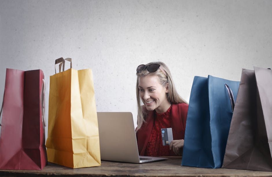 A joyful woman shopping online using a laptop with colorful shopping bags surrounding her.